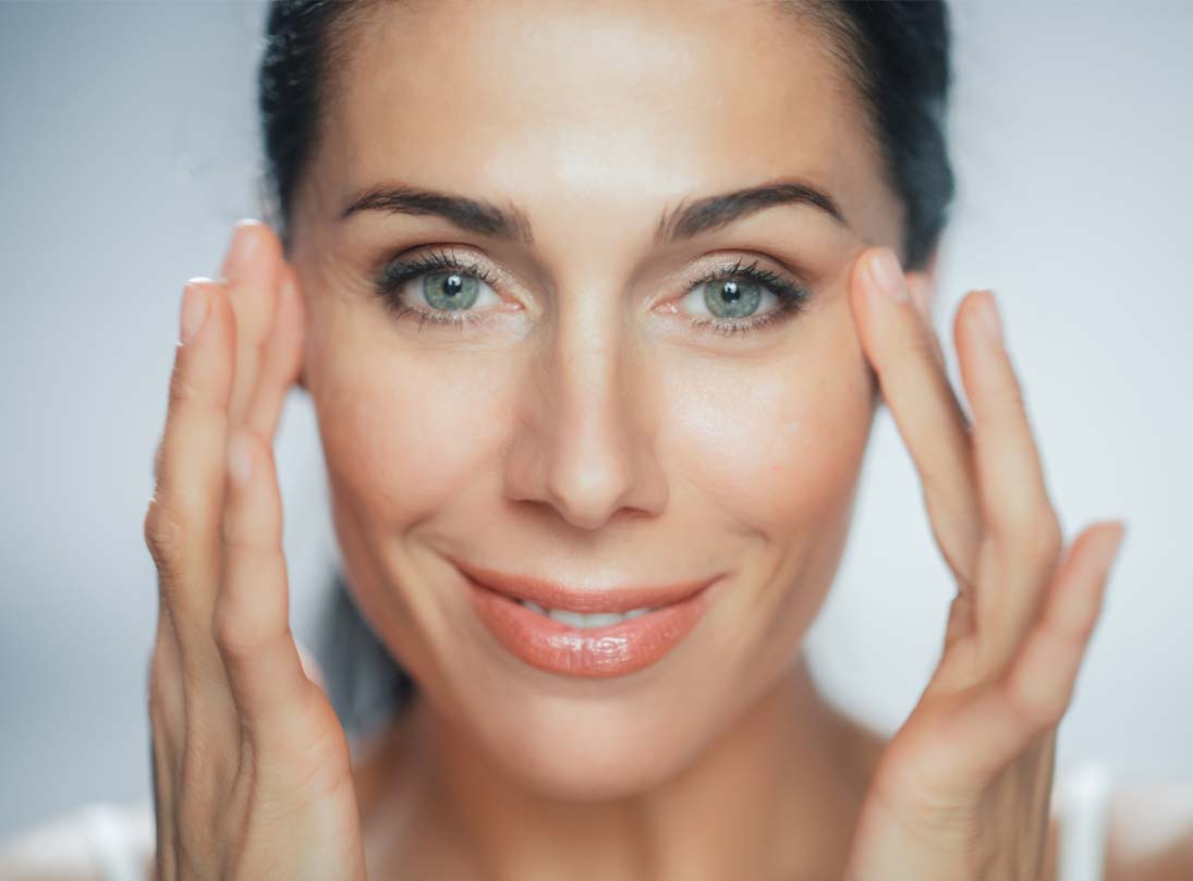 Beautiful Caucasian Woman Touches Her Perfect Face with Soft Skin, Smiling. Female Enjoying Her Beauty, High Self Esteem, Wellness. Natural Cosmetic Skincare Products.