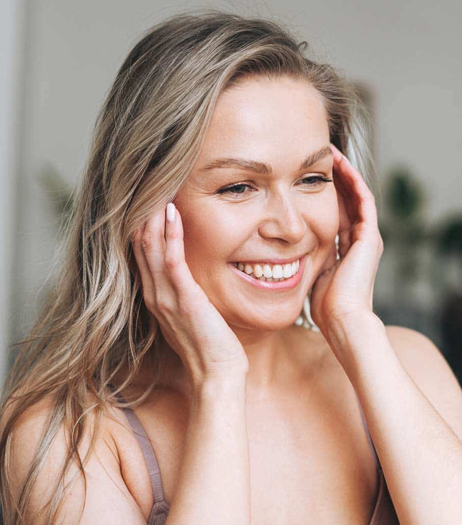 Blonde smiling woman with long hair does facial massage in underwear at bathroom, banner